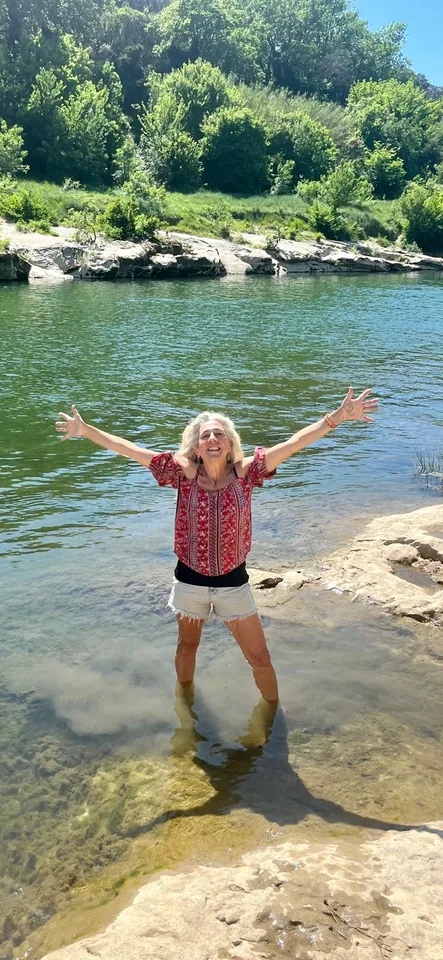 Hiker standing in the river after a hike with arms wide open.