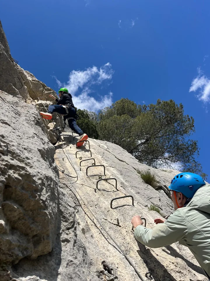 Guest climbing a via ferrata route under a bright blue sky.